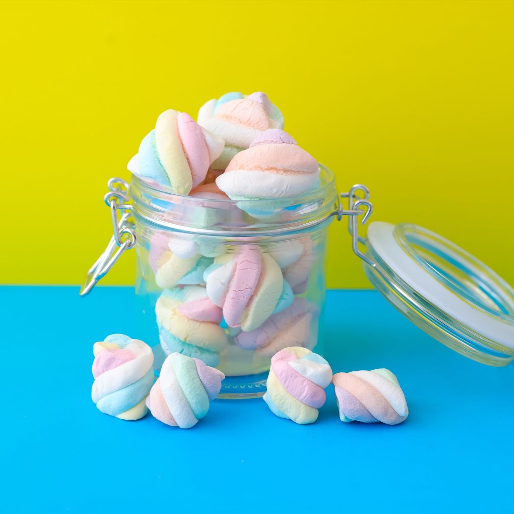 Pastel-colored marshmallows in a clear jar on a blue and yellow background