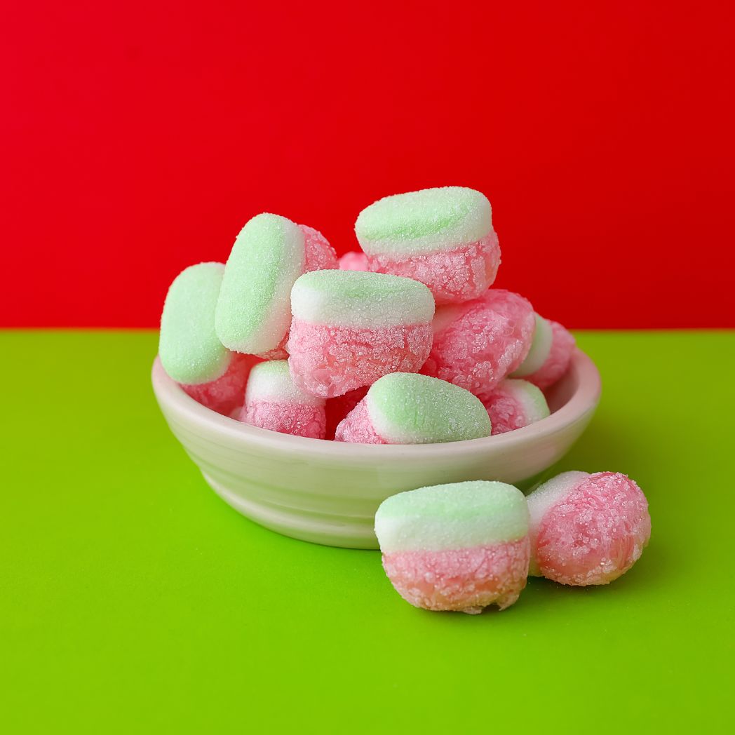 Pink and green gummy candies in a white bowl on a red and green background