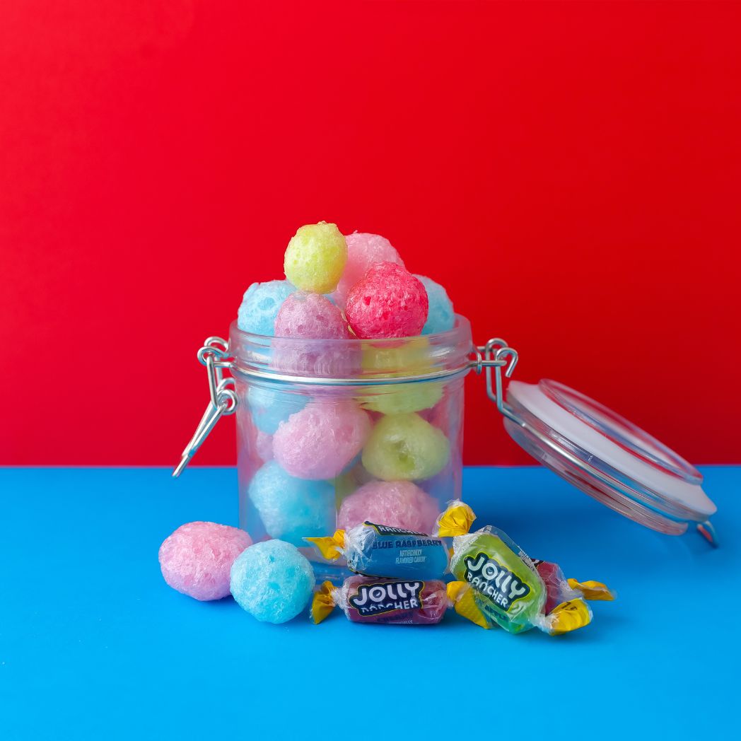 Colorful freeze dried jolly ranchers in a glass jar with a red and blue background