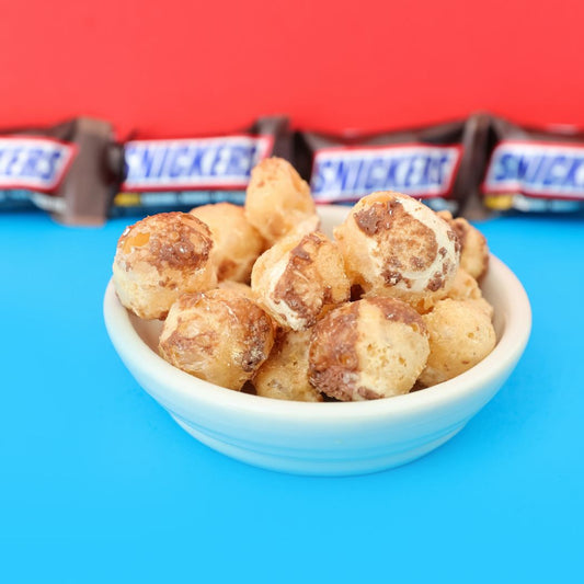 Bowl of Snickers bites with Snickers bars in the background on a blue and red background